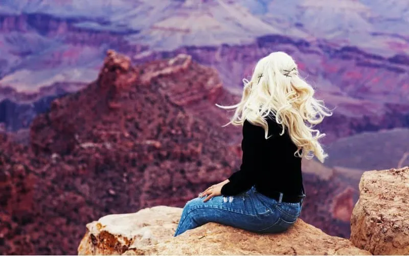Blonde woman sitting on brown cliff admiring the view during daytime