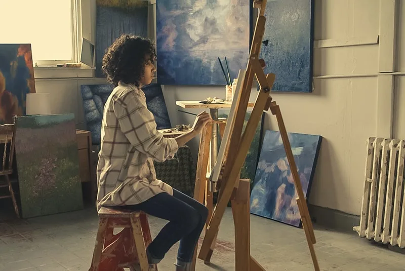 woman sitting on brown stool while painting