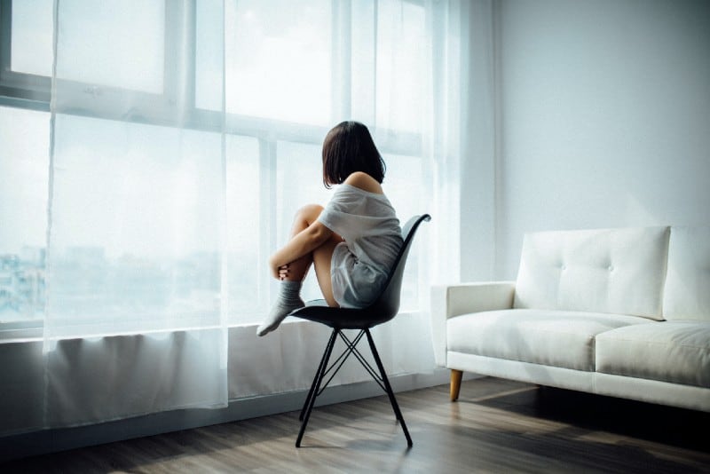donna seduta su una sedia nera vicino a una finestra con tenda bianca