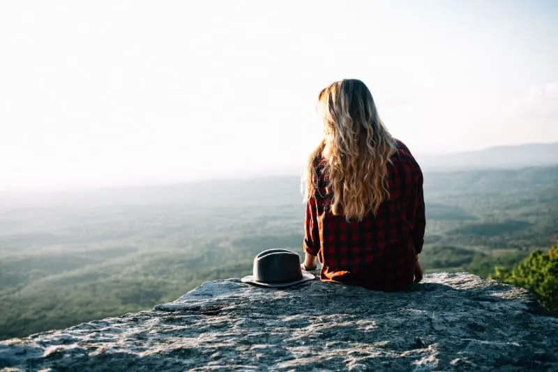 blonde woman in checked shirt sitting on cliff