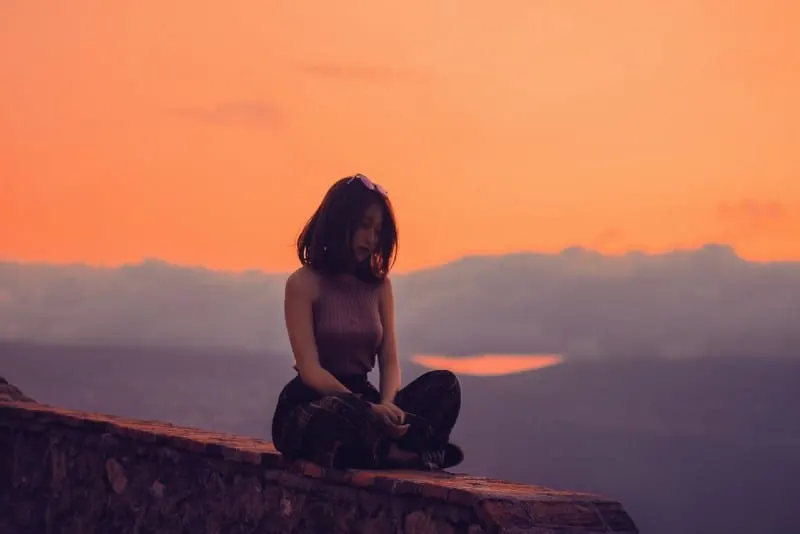 woman sitting on cliff during sunset
