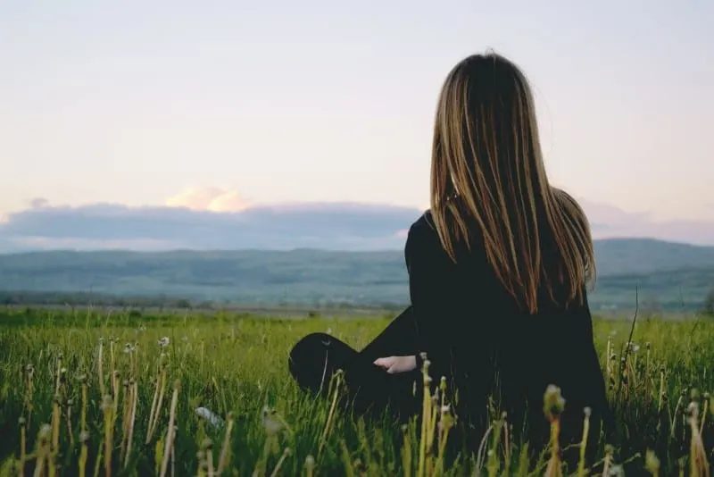 woman in black shirt sitting on grass looking at mountain