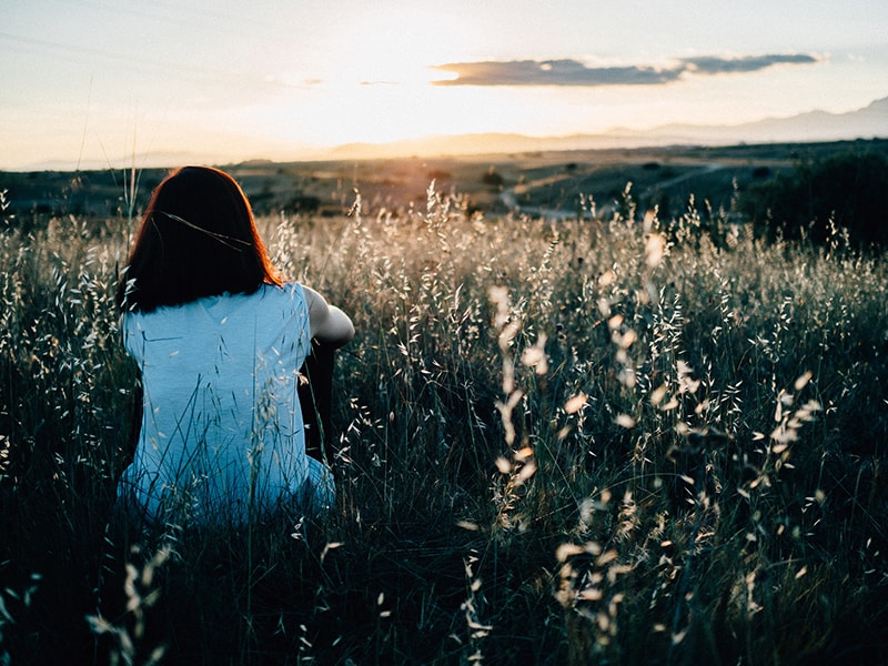 mujer sentada en el campo de hierba viendo la puesta de sol