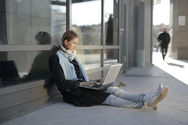 woman sitting on gray concrete floor and using laptop
