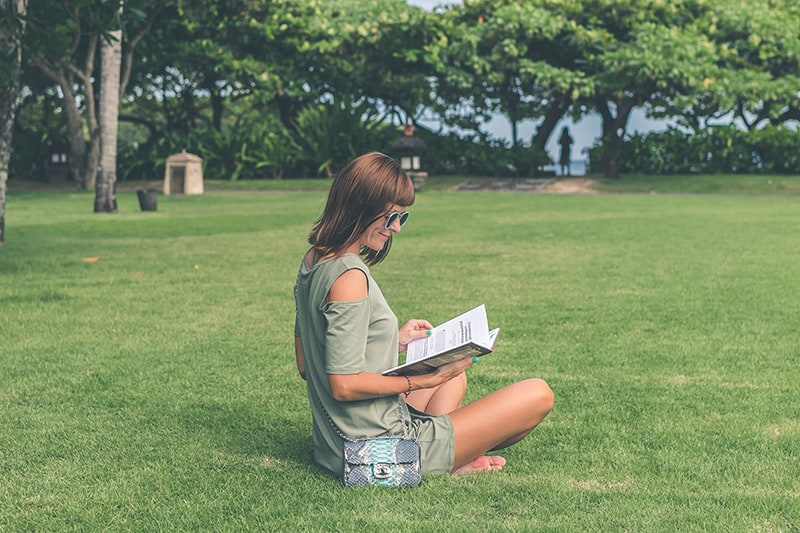 woman sitting on green grass while reading book
