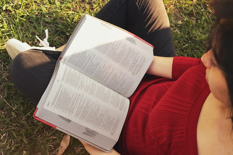 woman sitting on green grass field while reading book