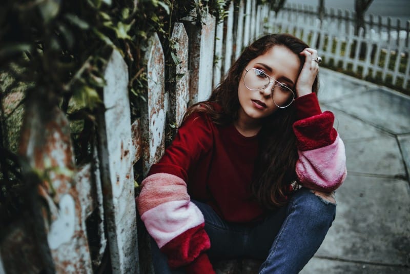 woman with red sweatshirt and eyeglasses sitting on ground