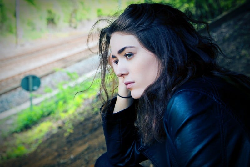 woman in black jacket sitting on ground at daytime
