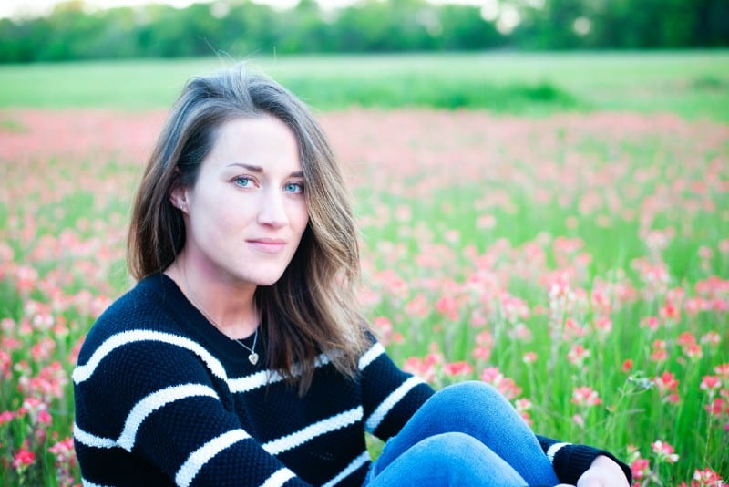 donna con maglione a righe seduta su un campo di fiori