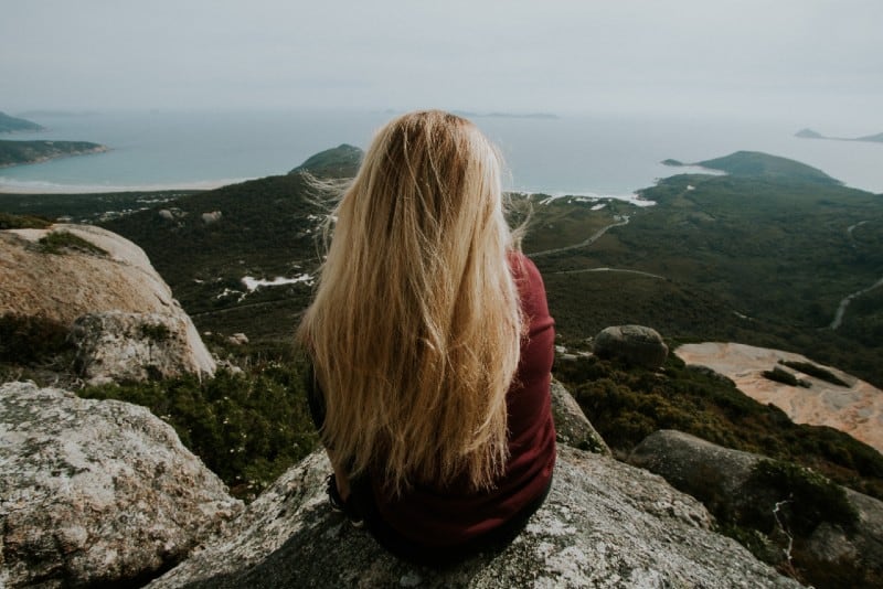 donna bionda seduta in cima a una collina che guarda il mare