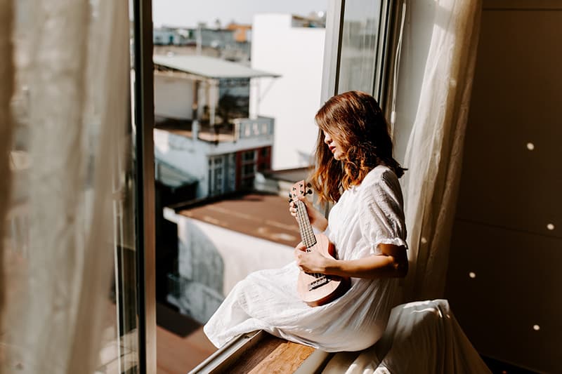 mujer sentada en la ventana dentro de la habitación y tocando un instrumento