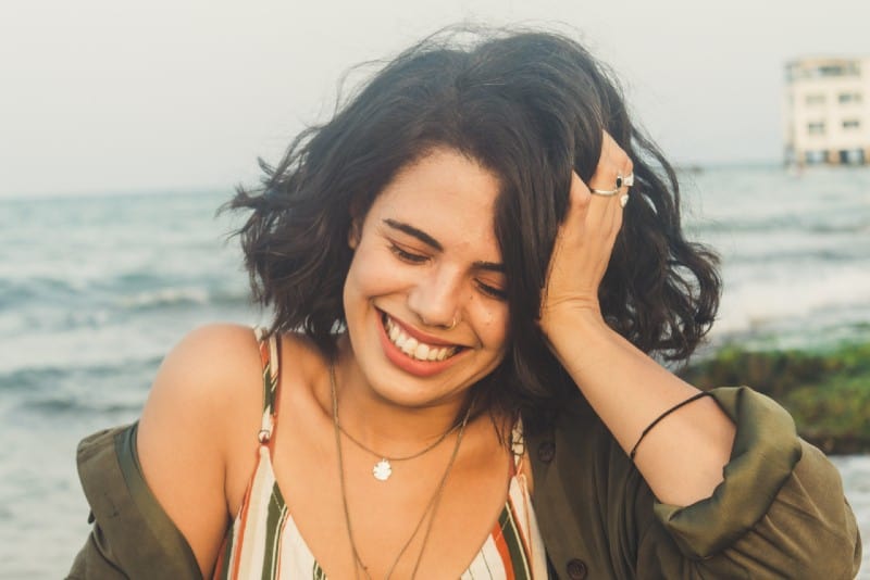 woman with necklace touching hair and smiling