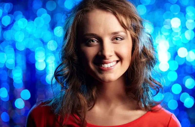 woman smiling after party wearing orange top in shiny blue background