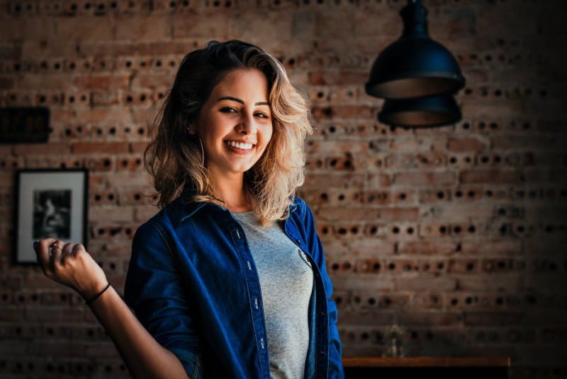 woman in blue denim shirt smiling near wall