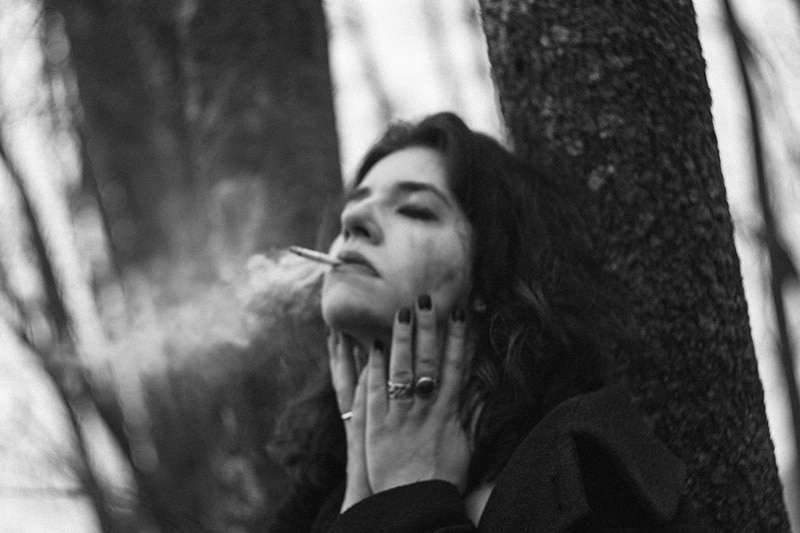 donna che fuma una sigaretta appoggiata a un albero
