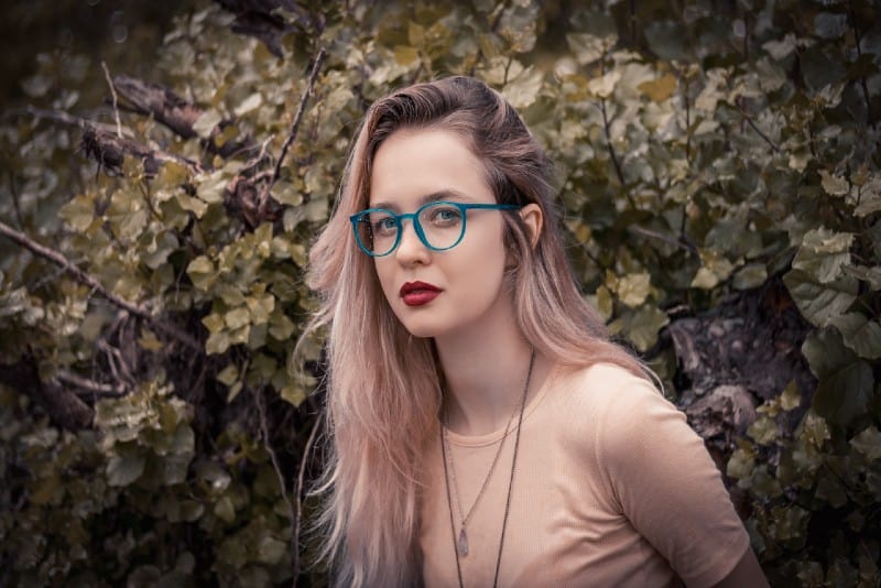 mujer con gafas y pintalabios rojo de pie cerca de una planta