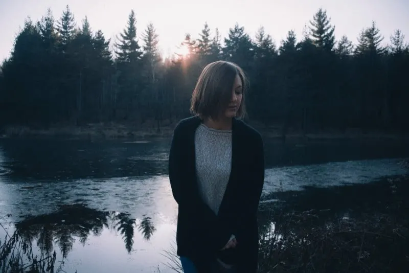 woman in black cardigan standing by the lake