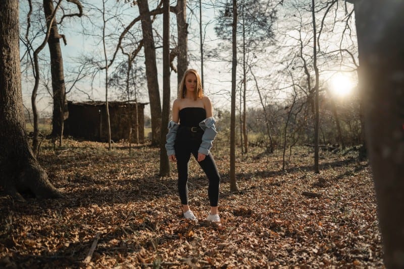 mulher de camisola e calças pretas numa floresta