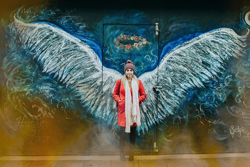 woman standing in front of a street art wall with spread wings grafitti