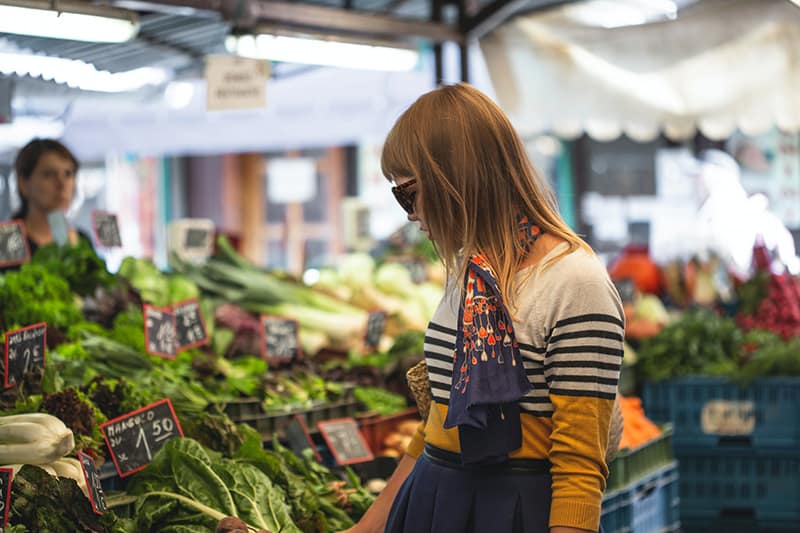 Donna in piedi davanti a verdure al mercato durante il giorno