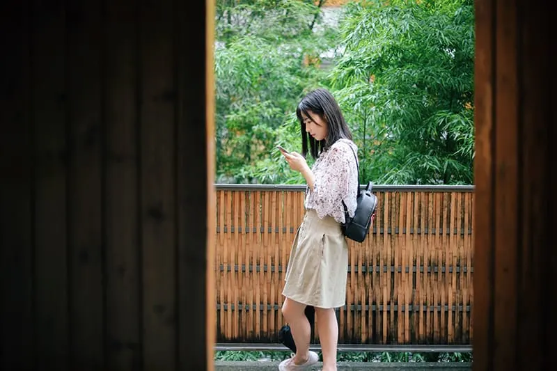 woman standing near brown and black wooden balcony while using smartphone