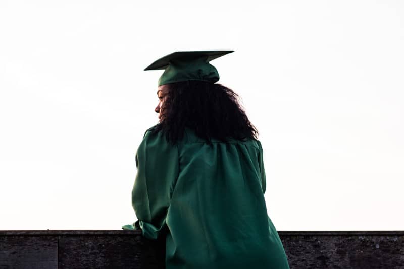 mulher de pé em frente a uma vedação de betão com uniforme académico