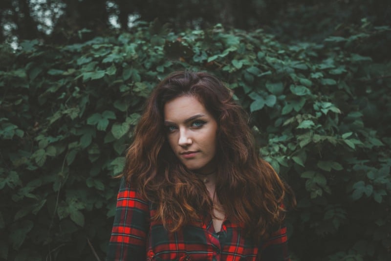 woman in checked shirt standing near green leaves