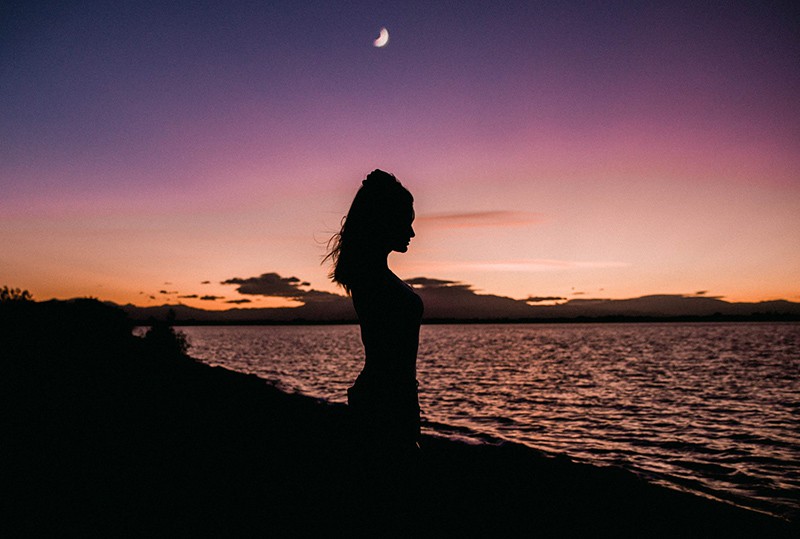 mujer de pie cerca del agua durante la puesta de sol