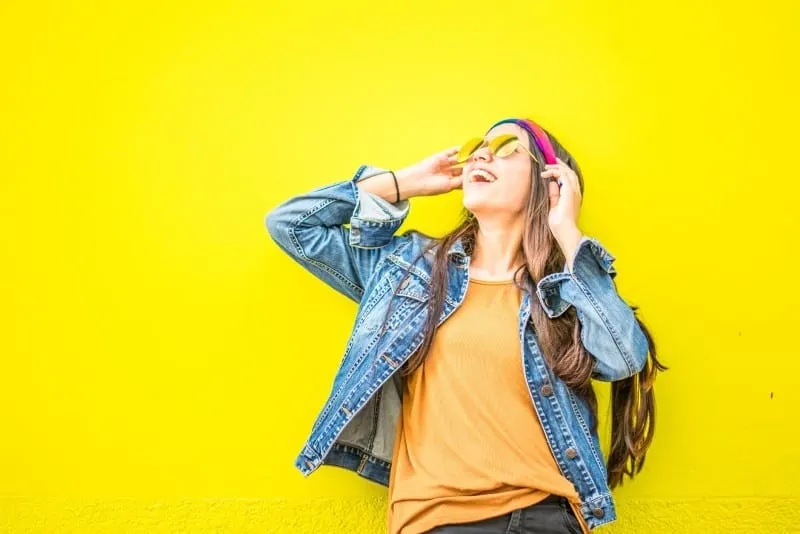 woman with sunglasses standing near yellow wall