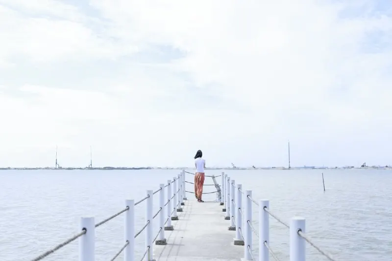 woman in white shirt standing on dock looking at water
