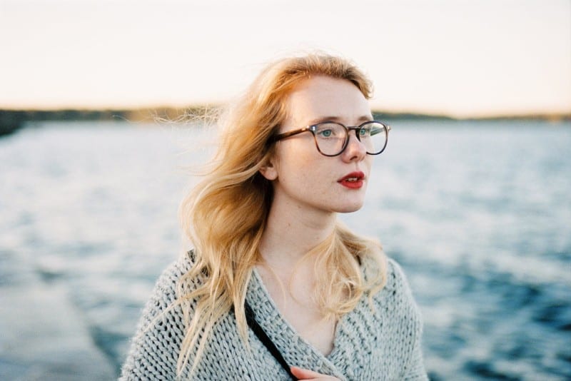 woman in gray knit cardigan and eyeglasses standing near water