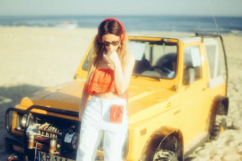 woman standing near yellow vehicle while listening music on a portable media player