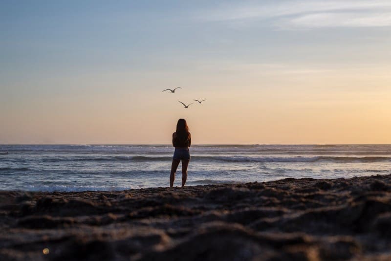 donna in piedi sulla riva che guarda l'oceano