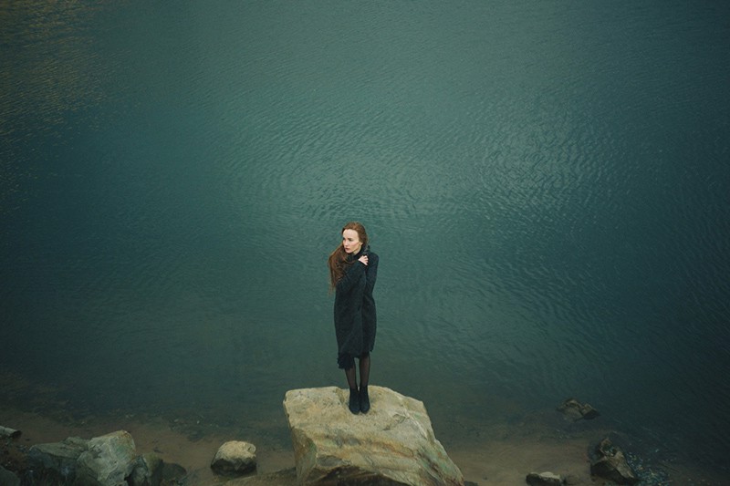 mujer de pie sobre la roca cerca del agua