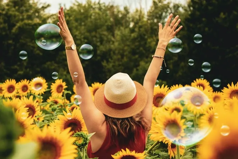 woman with hat surrounded by sunflowers