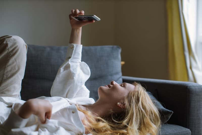 donna che si scatta un selfie indossando un top bianco mentre è sdraiata su un divano