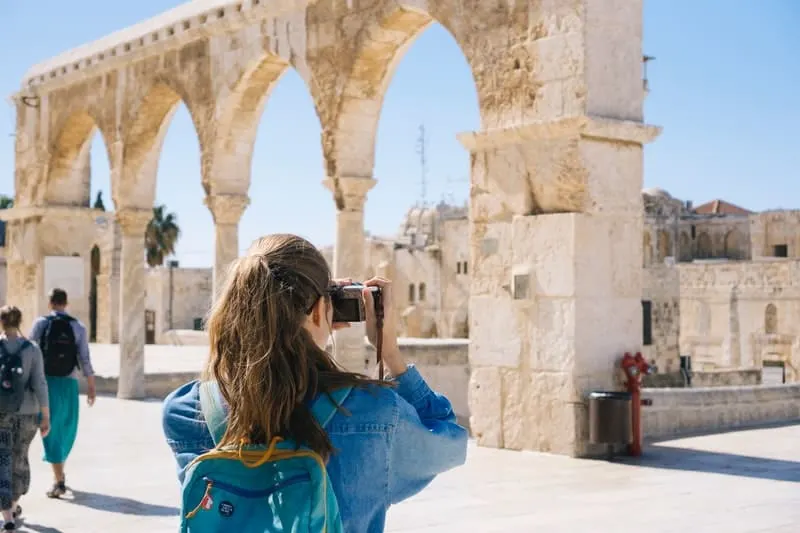 woman taking pictures of ruins wearing blue top and carrying blue pack