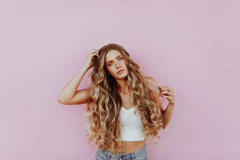 woman standing near pink wall and touching hair