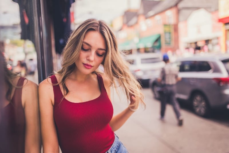 blonde woman in red top touching her hair