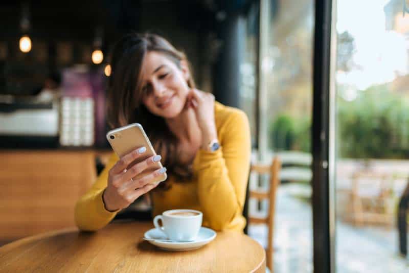 mulher a escrever no telemóvel num café