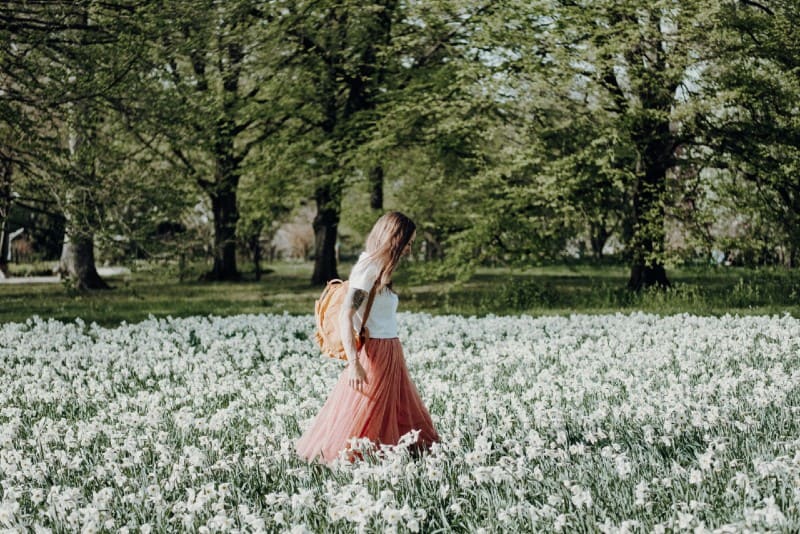 woman with backpack walking through flower field