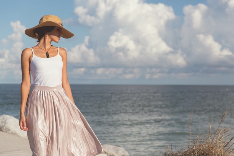 donna con cappello e gonna rosa che cammina vicino al mare