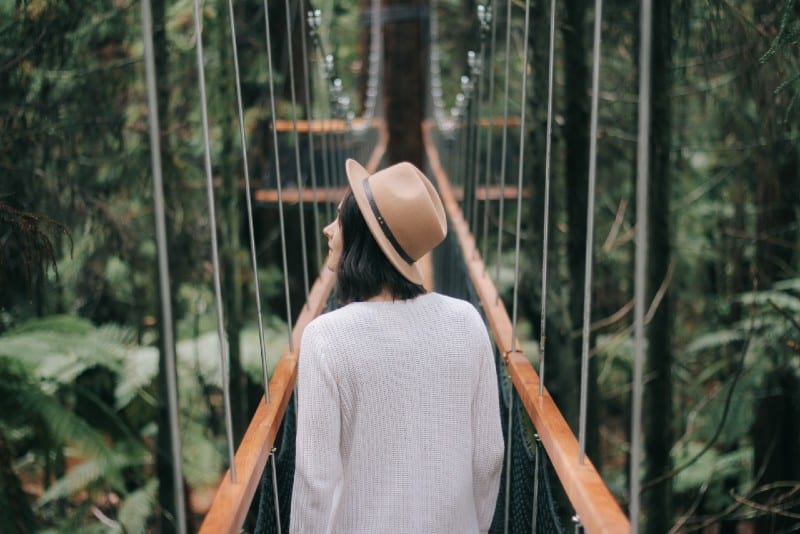 donna con cappello che cammina su un ponte guardandosi intorno