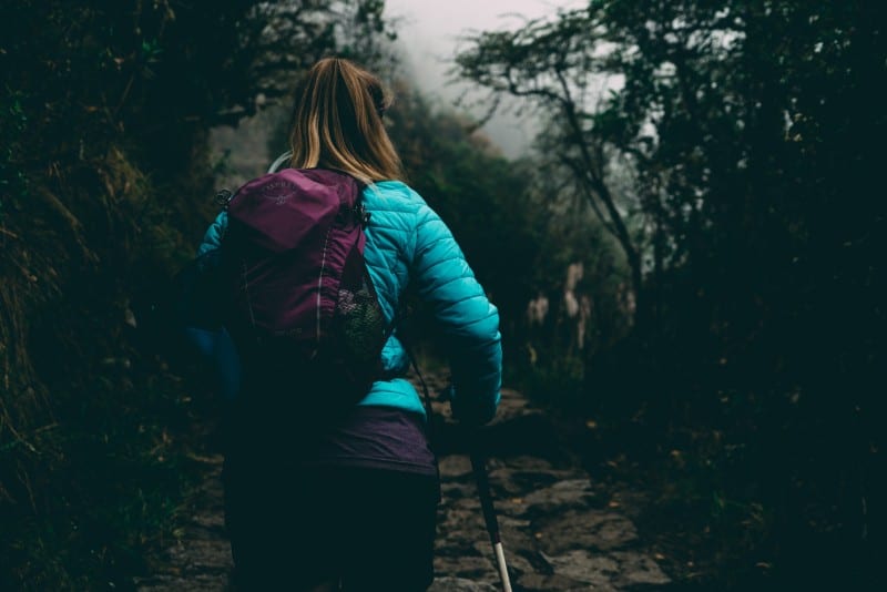 mujer con chaqueta de burbujas caminando por un sendero entre bosques