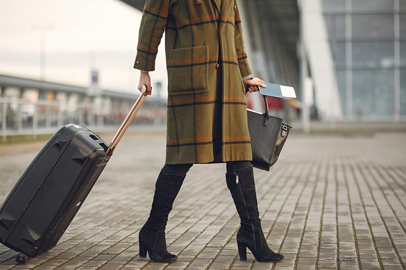 woman wearing a coat holding black luggage bag