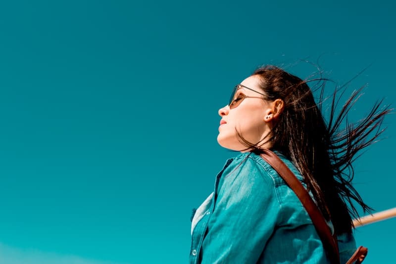 mujer con top azul y gafas de sol mirando al cielo azul