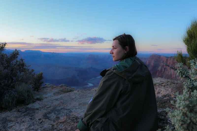 donna che indossa una giacca marrone seduta in cima alle montagne