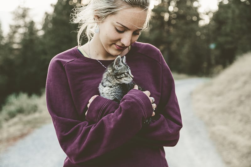 woman wearing purple sweatshirt hugging grey kitten