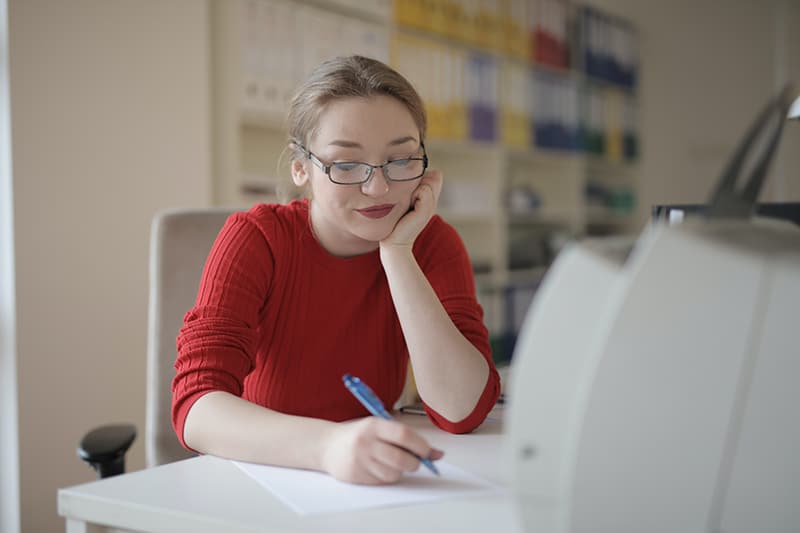 donna con maglione rosso che scrive su un foglio