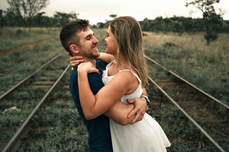 woman wearing sleeveless embraced by a man in the middle of a railway